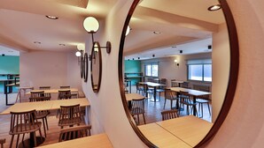 A spacious dining area with multiple tables and chairs, a large mirror on the wall, and recessed ceiling lights.