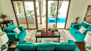 A living room with teal sofas, a wooden coffee table, and a view of a pool and outdoor seating area.