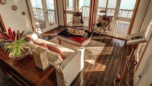 A spacious living room with a large window overlooking the ocean, a wooden floor, and a cozy seating area with a sofa and chairs.