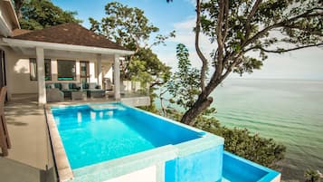 A swimming pool with a view of the sea, a covered patio, and a house with a tiled roof.