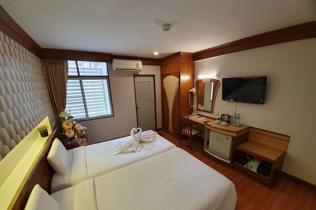 A hotel room with a bed, a desk, a TV, a mirror, and a window with blinds.