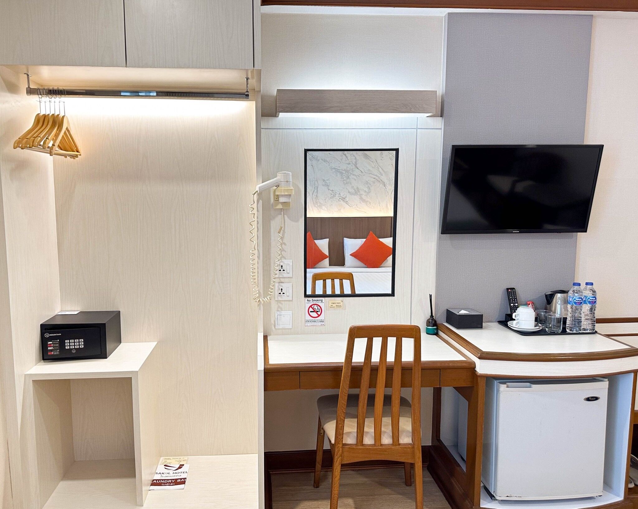 A hotel room with a desk, chair, television, and a small refrigerator.