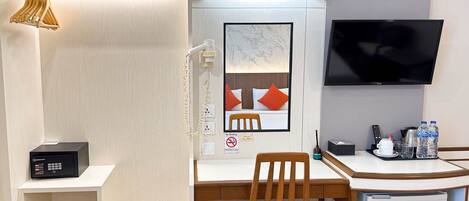 A hotel room with a desk, chair, television, and a small refrigerator.