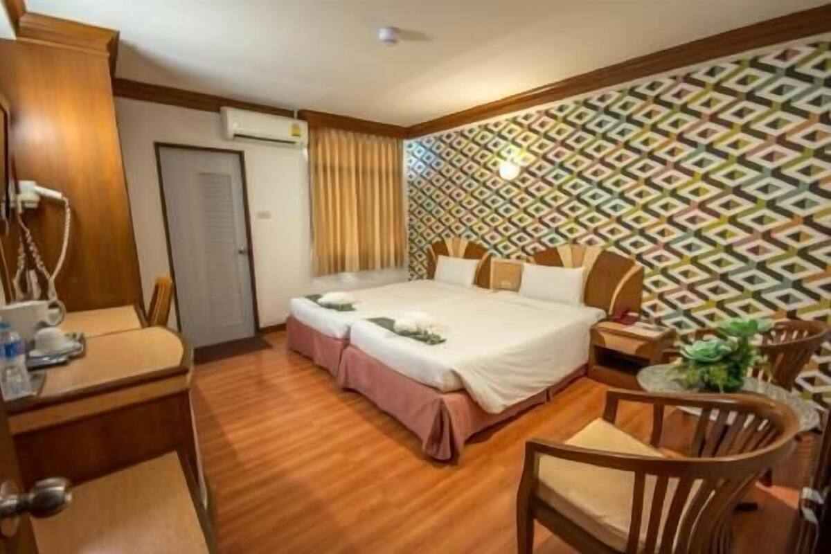 A hotel room with a bed, bedside table, chair, desk, and an air conditioning unit.