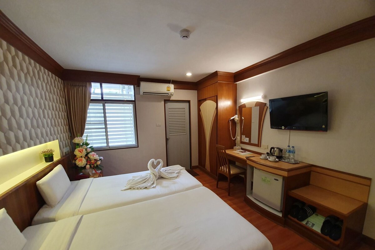 Een hotelkamer met twee bedden, een bureau, een televisie, een spiegel en een kleine kitchenette.