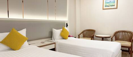 A hotel room with two beds, a small table, two chairs, a painting on the wall, and a wooden ceiling trim.