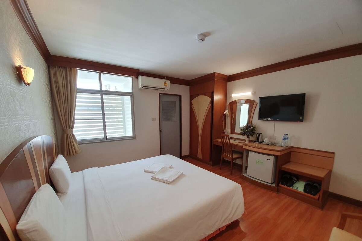 Een hotelkamer met een bed, bureau, stoel, televisie en een kleine koelkast.