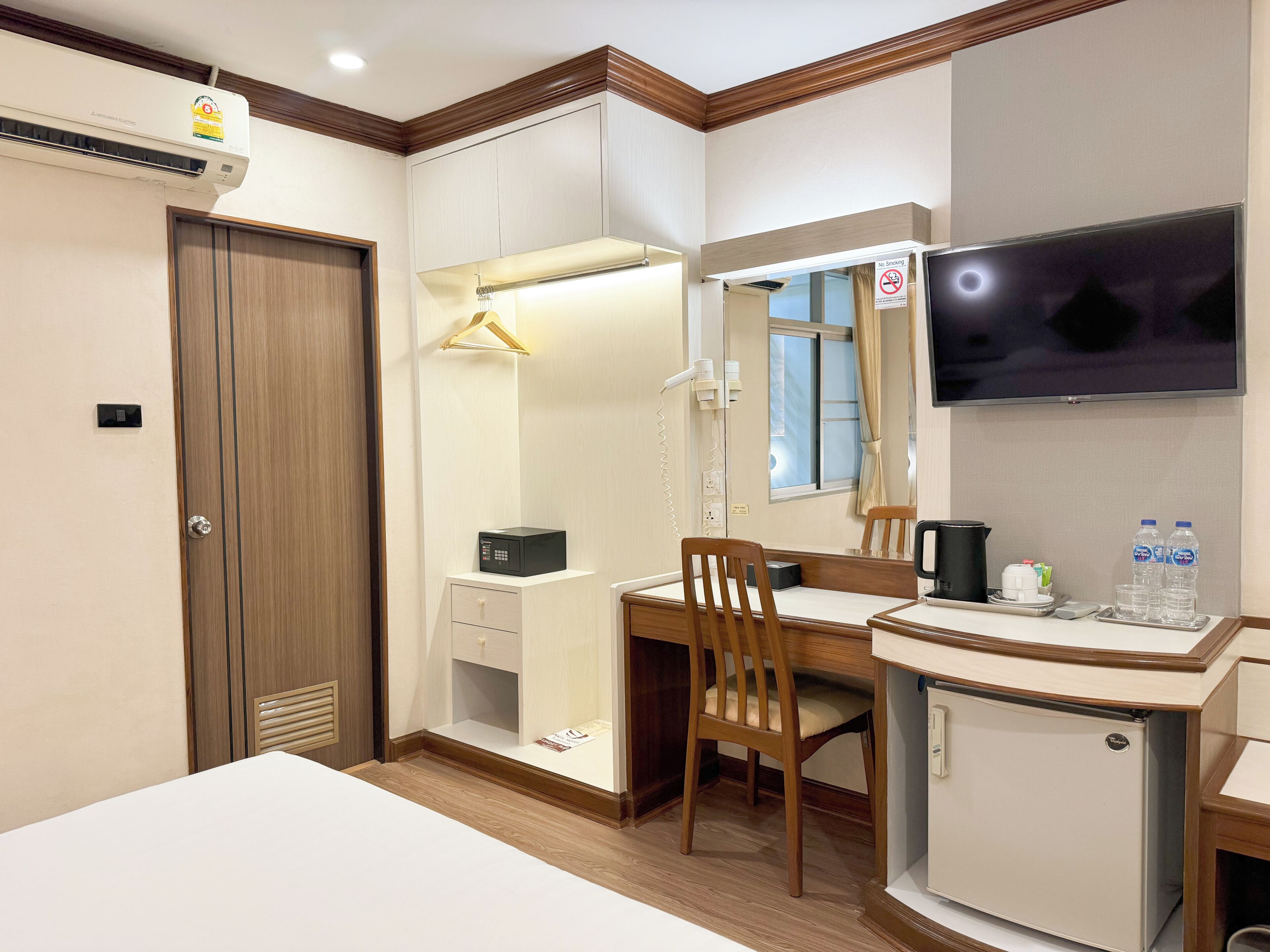 Een hotelkamer met een bed, een bureau, een stoel, een kledingkast, een spiegel, een televisie en een minibars.