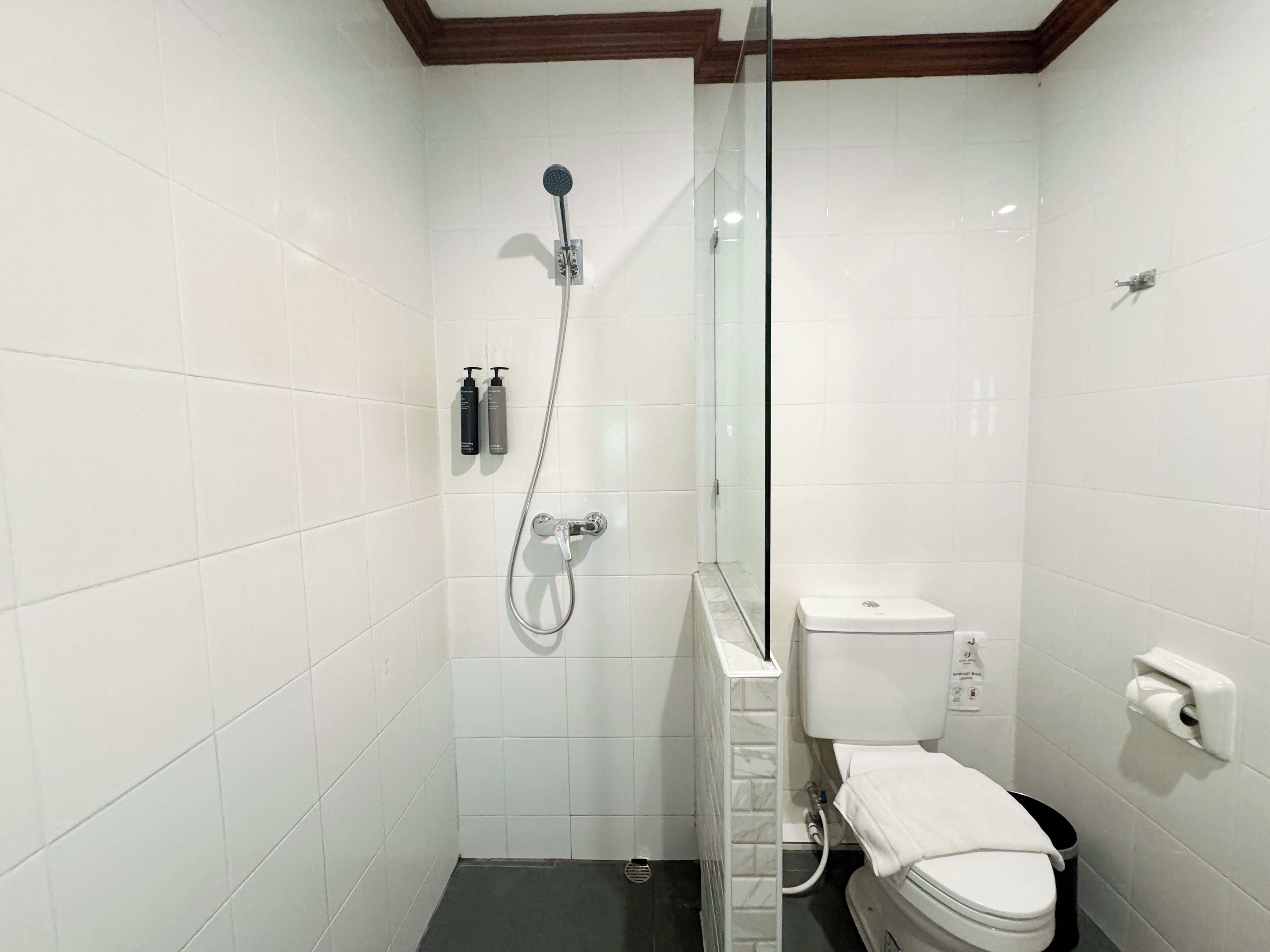 Un baño pequeño y moderno con azulejos blancos, mampara de vidrio, inodoro y toallero.