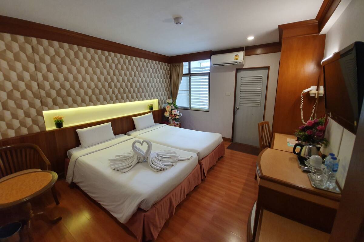 A hotel room with two beds, a desk with a chair, a TV, and a window with blinds.