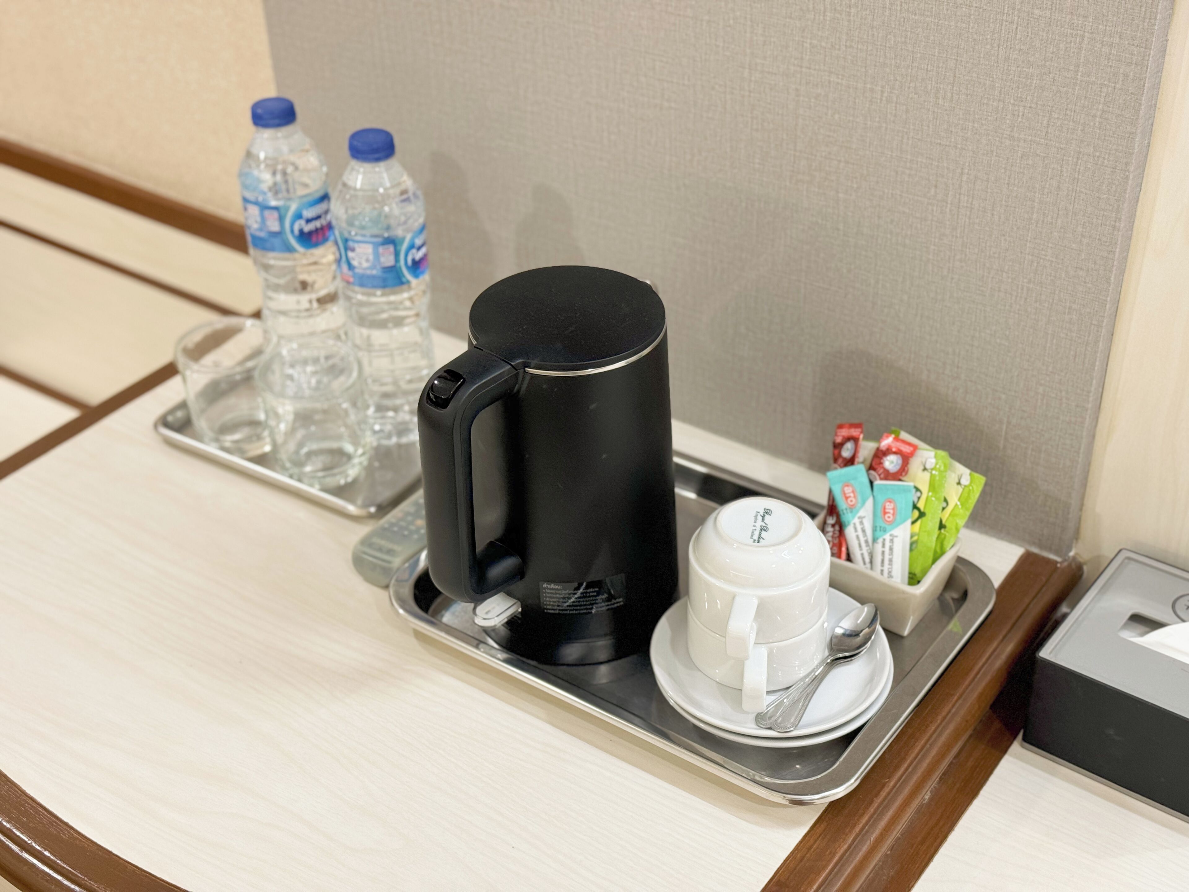A tray with a black coffee maker, a white cup and saucer, two water bottles, and a box of tea bags.