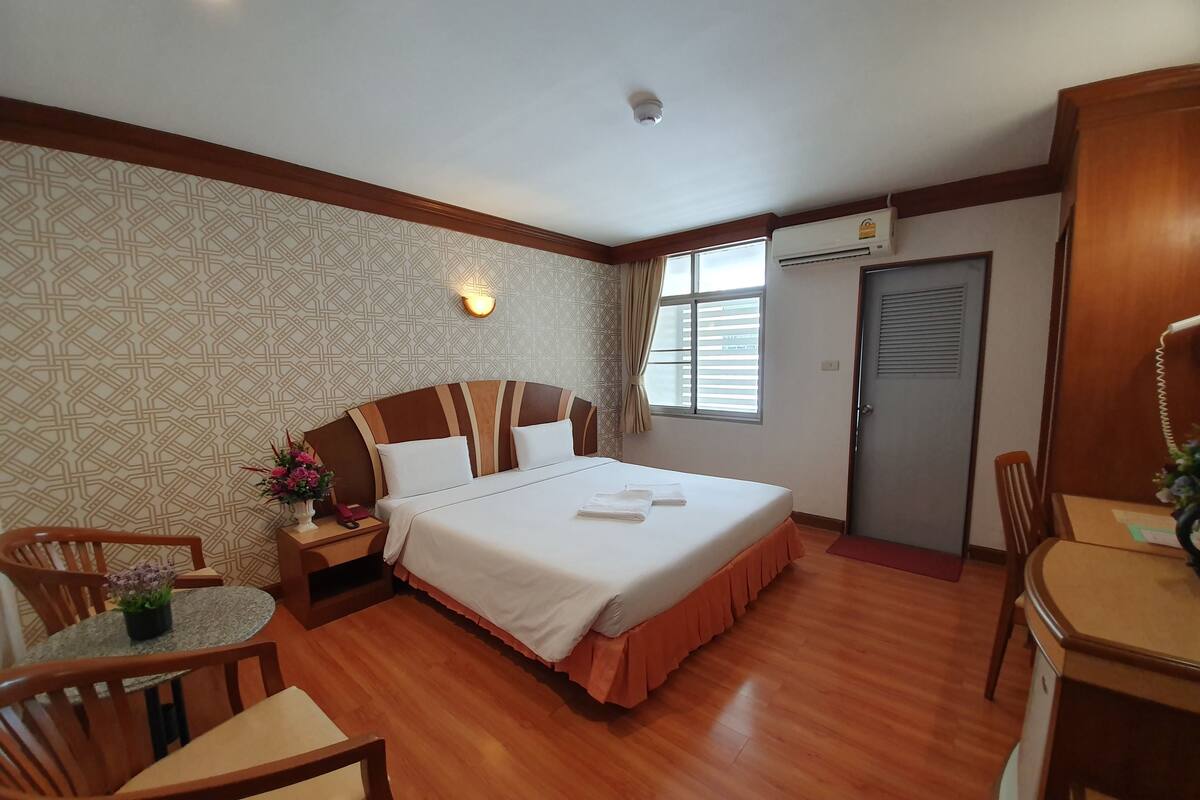 A hotel room with a large bed, a desk, a chair, and a small table.