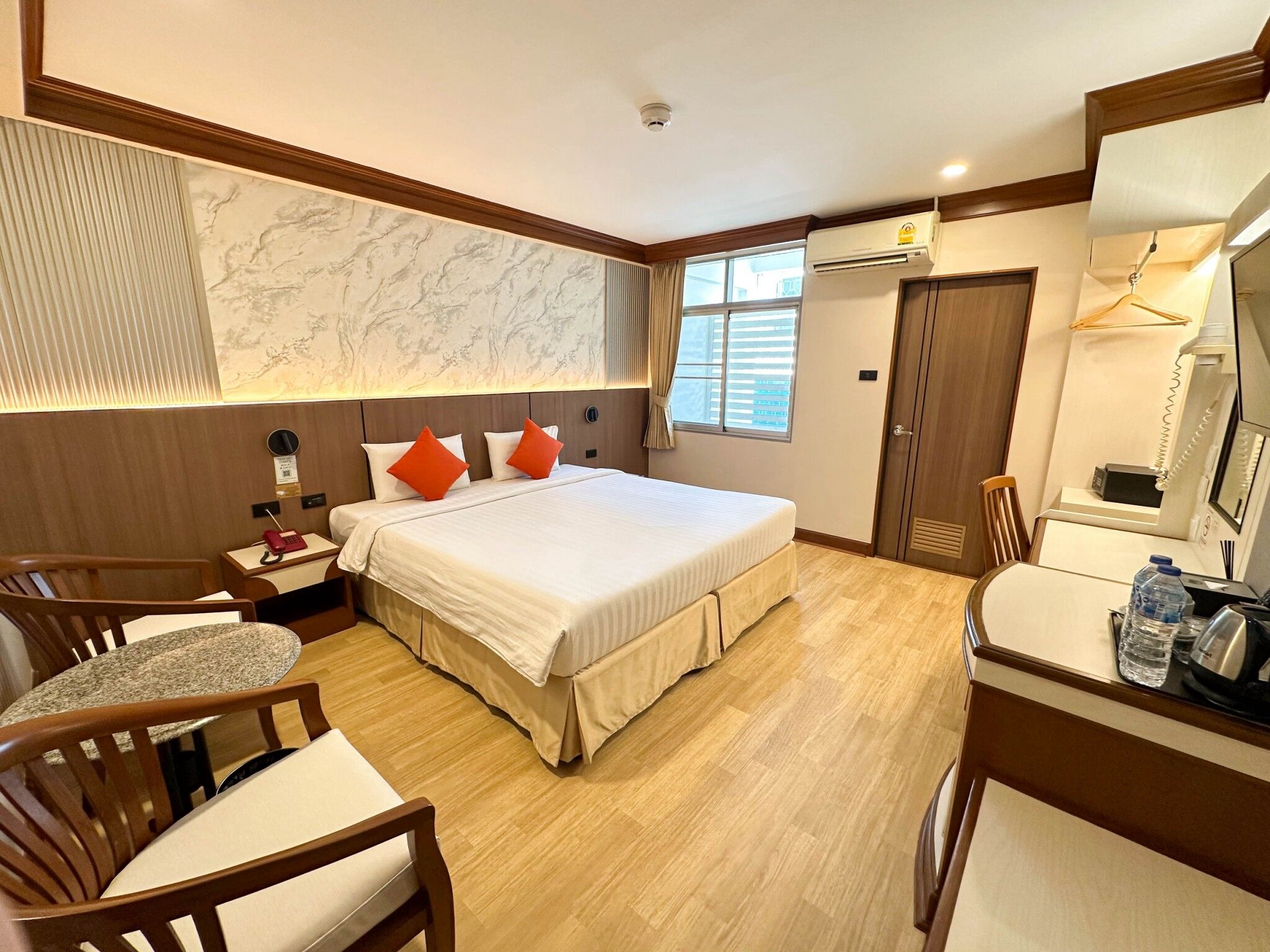 Een hotelkamer met een bed, nachtkastje, stoel, bureau en een spiegel.