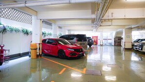 Een parkeergarage met meerdere auto's, waaronder een rode sportauto, en een schone, goed verlichte omgeving met overheadleidingen en een gepolijste vloer.