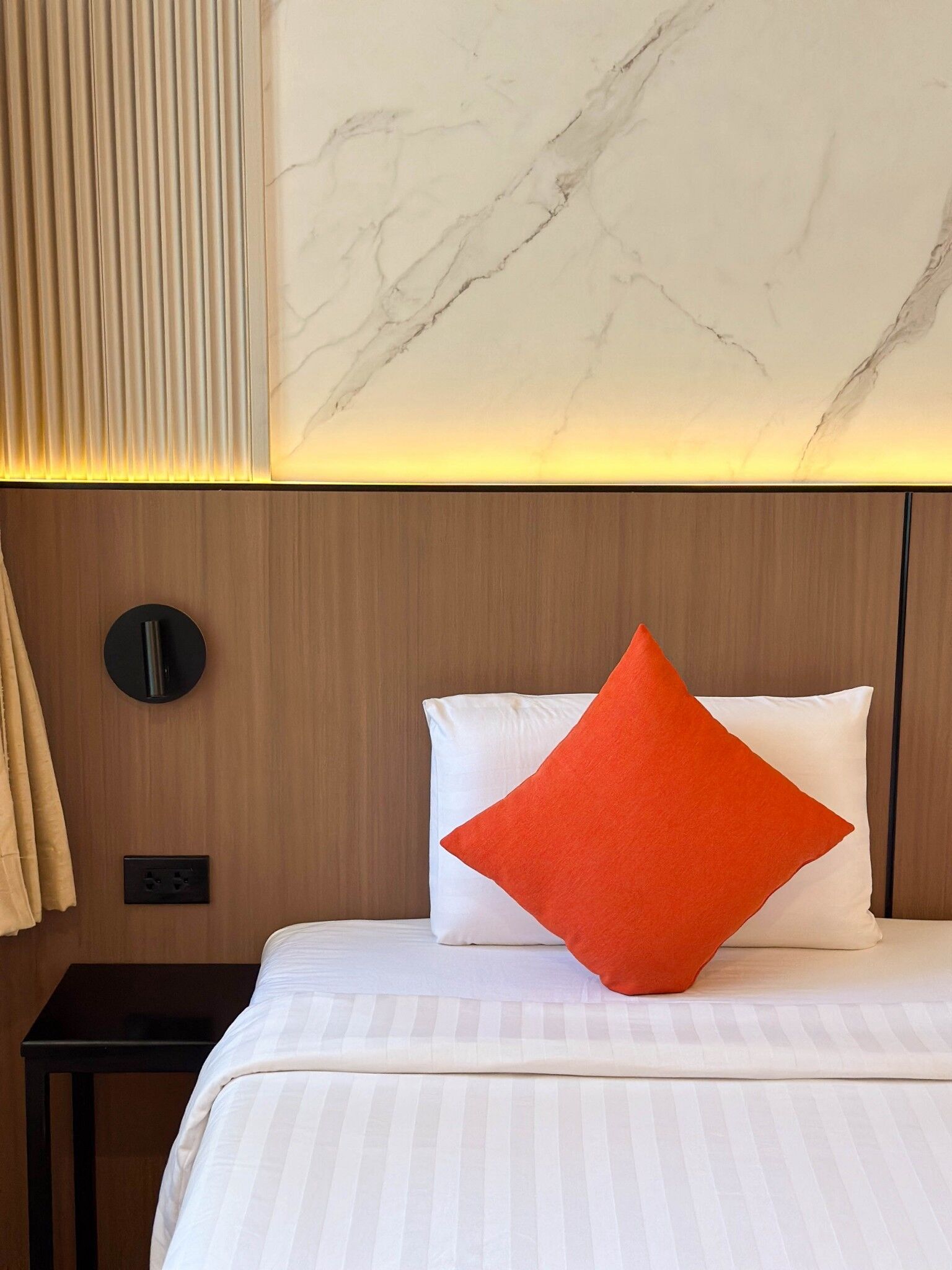 Una habitación de hotel con una cama, una mesita de noche, una lámpara de pared y una pared con diseño de mármol.