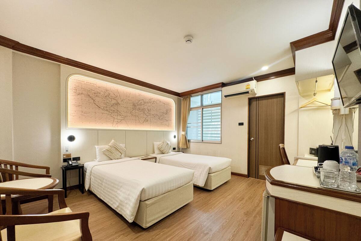 A hotel room with two beds, a desk, a chair, a map on the wall, and a television.
