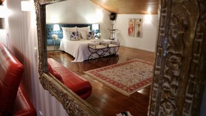 A bedroom with a large mirror, a bed with a blue headboard, a bedside table, and a red leather chair. - Quinta da Terrincha (Torre de Moncorvo)