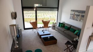 A modern living room with a sofa, two armchairs, a coffee table, and a side table. There is a large window with a view of a green landscape. - Quinta da Terrincha (Torre de Moncorvo)