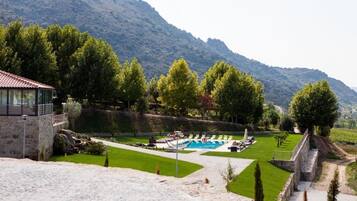 A pool area with a stone building, surrounded by trees and hills.