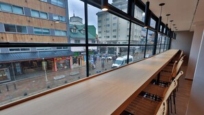 Una barra de madera larga con sillas de mimbre y vista a la calle.