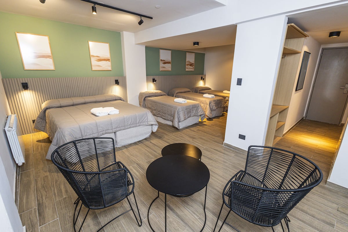 A modern hotel room with a large bed, two smaller beds, a round table, and two chairs.