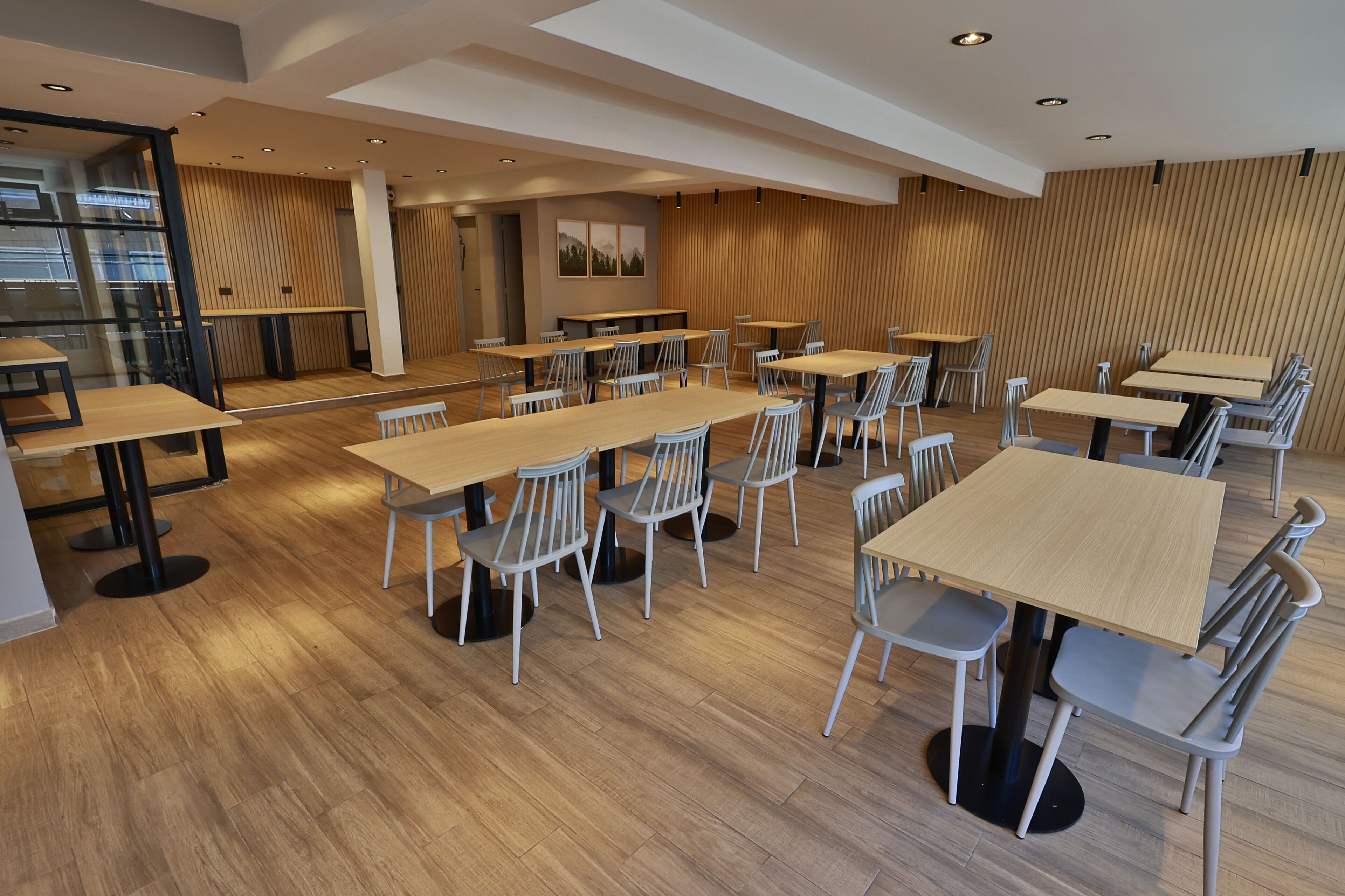 A spacious dining area with multiple tables and chairs, wooden flooring, and a modern interior design.