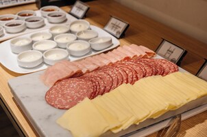 A charcuterie board with various meats and cheeses, accompanied by small bowls of condiments.