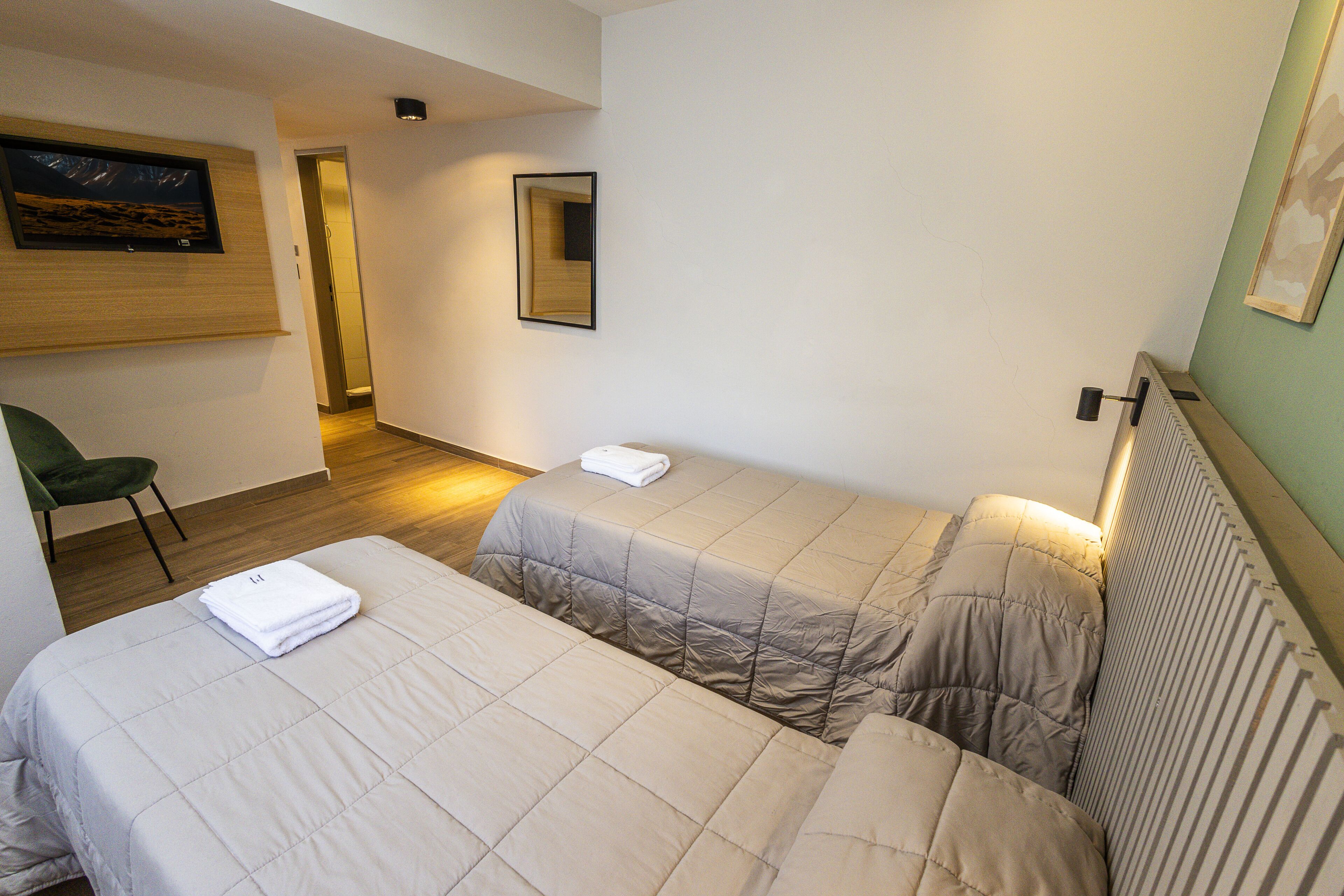Habitación de hotel con dos camas, una silla y un cuadro en la pared.