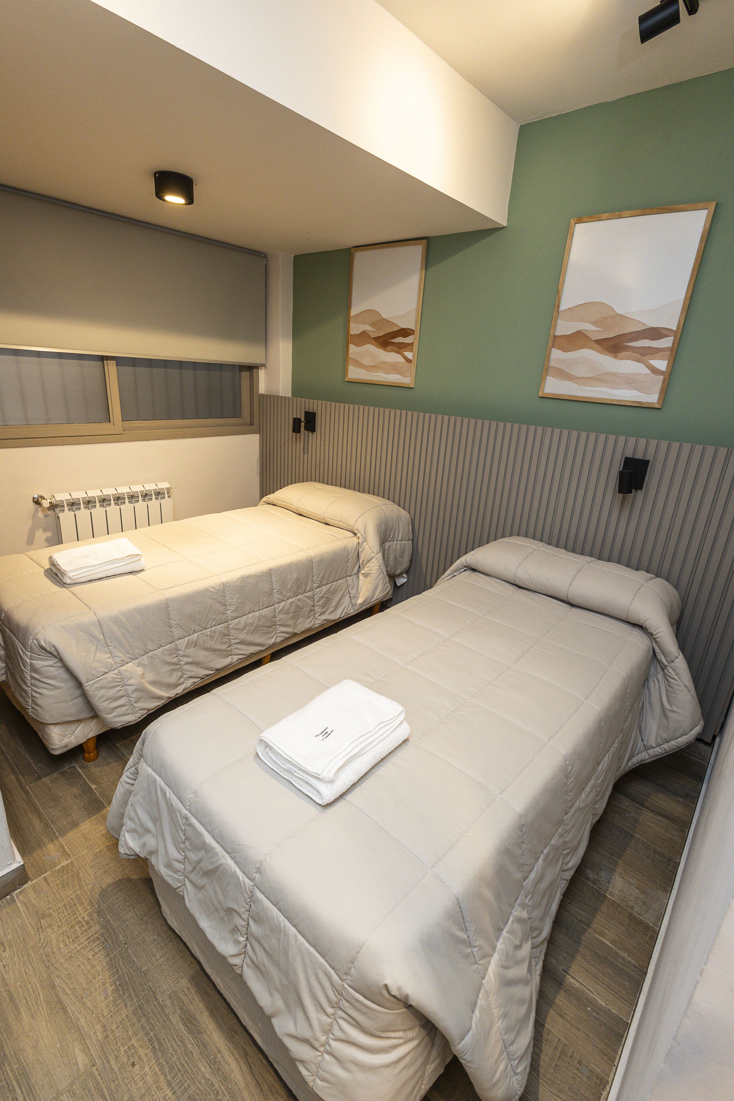 A room with two single beds, a radiator, and two framed pictures on the wall.