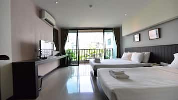 Habitación de hotel con dos camas, un escritorio con computadora, televisor y balcón con vista a edificios.