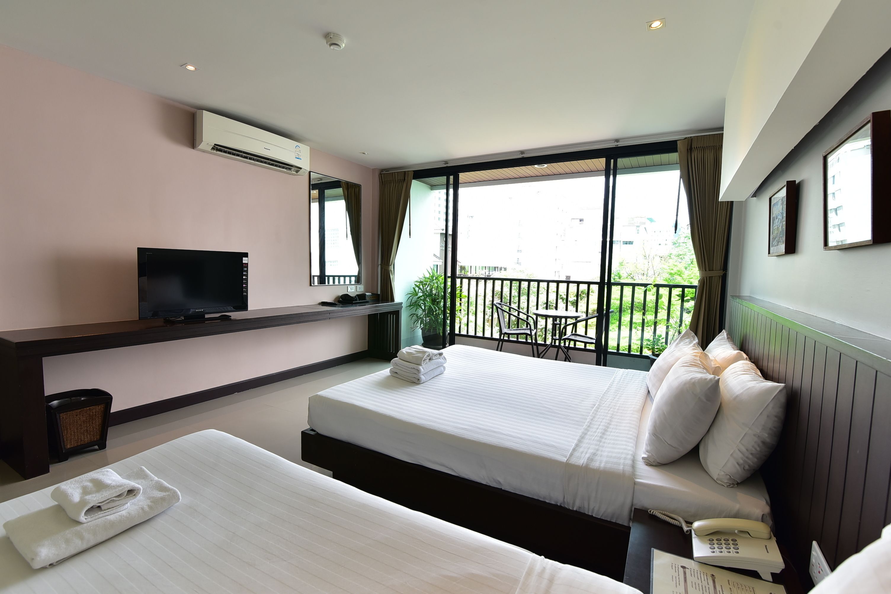 Habitación de hotel con dos camas, televisión, teléfono y balcón con vistas.