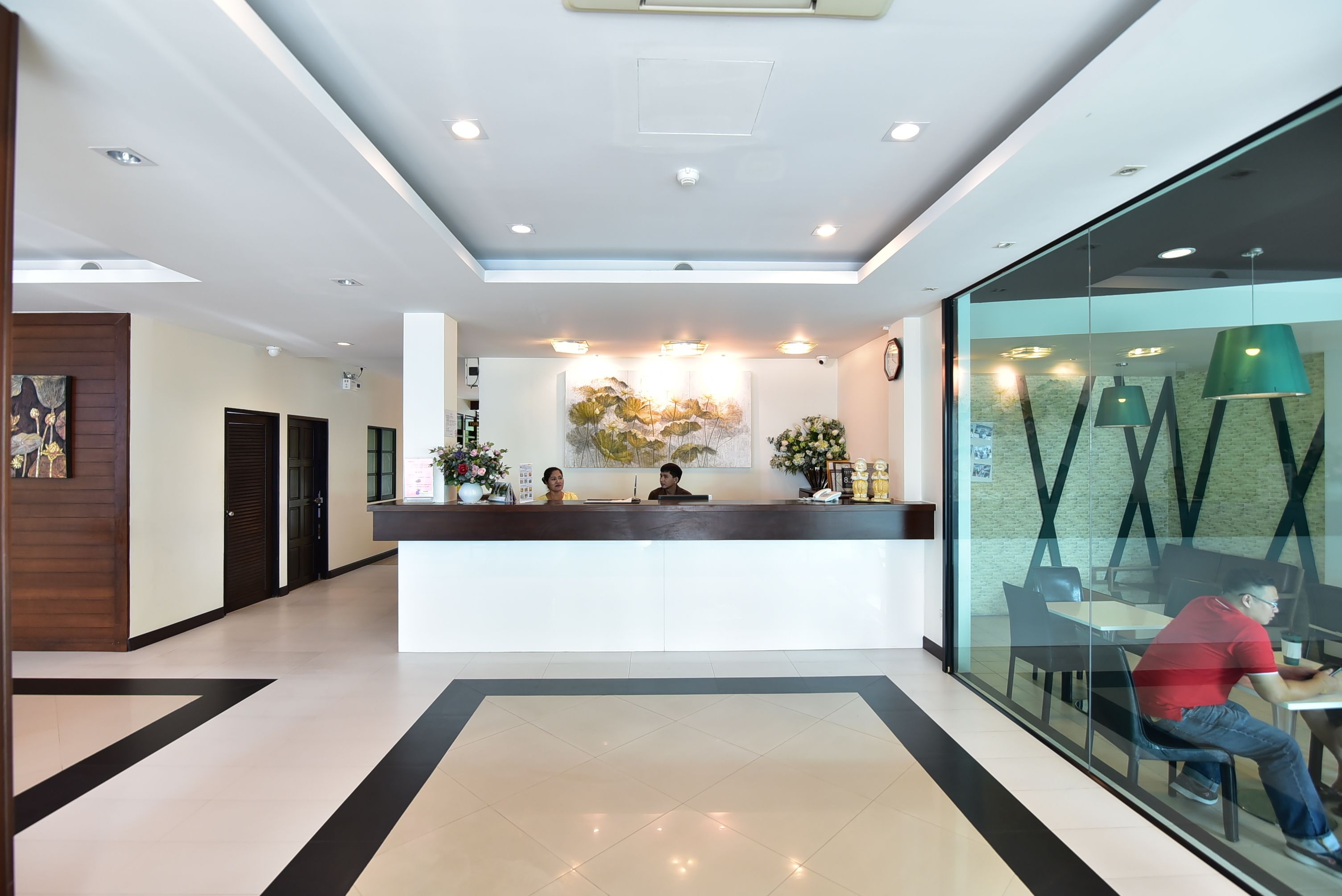 A modern reception area with a glass partition, a reception desk, and a seating area with a person using a laptop.