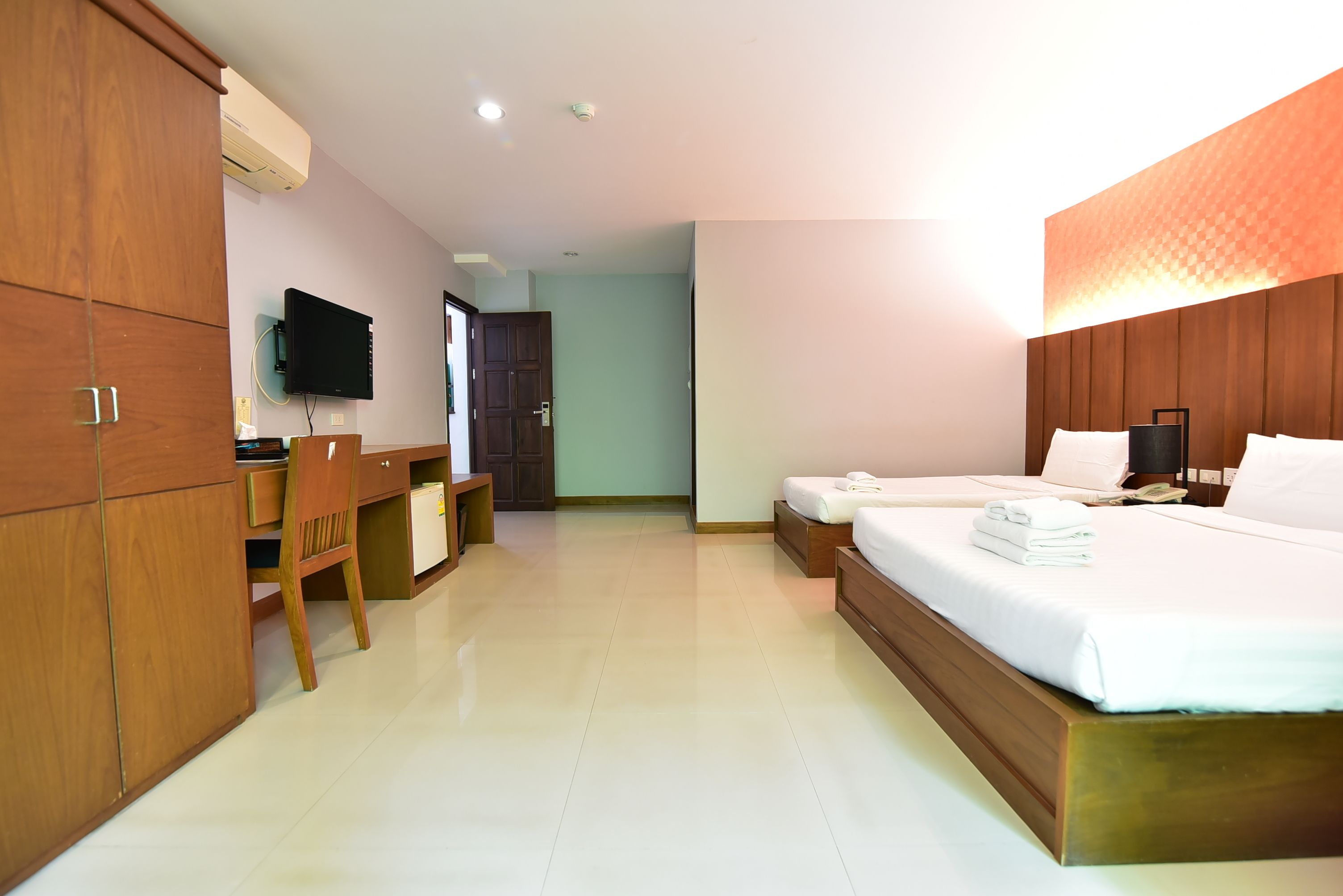 A hotel room with a wooden wardrobe, a desk, a bed with white linens, and a television mounted on the wall.