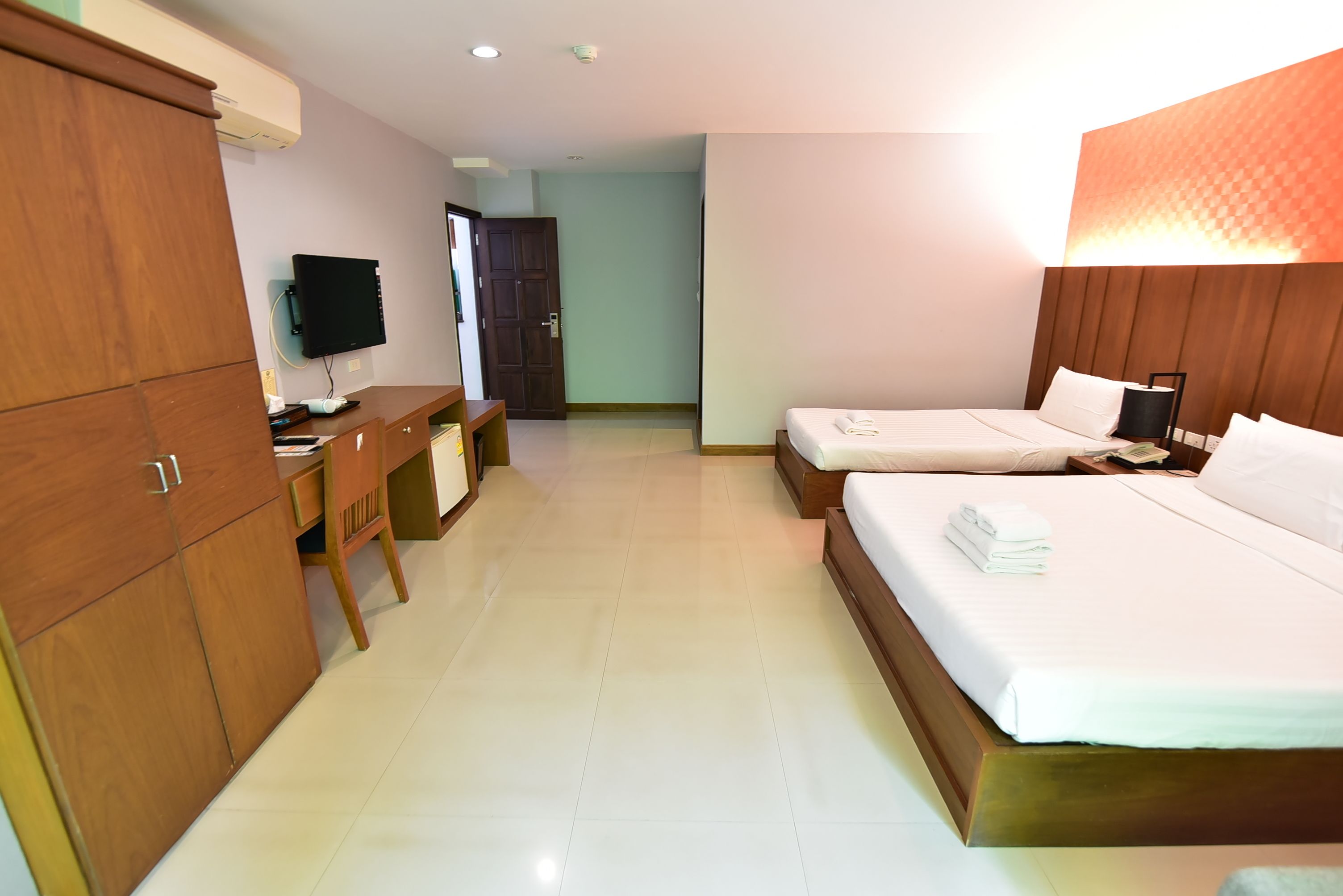 A hotel room with two beds, a desk, a TV, and a wardrobe.