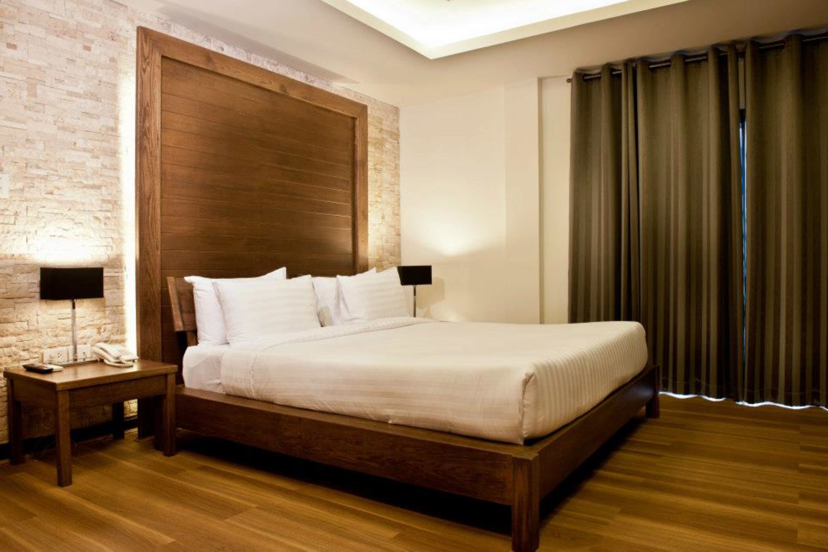 A neatly made bed in a room with a brick wall, wooden headboard, and a wooden floor.
