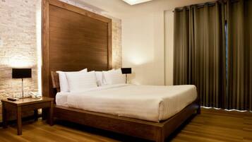 A neatly made bed in a room with a brick wall, wooden headboard, and a wooden floor.