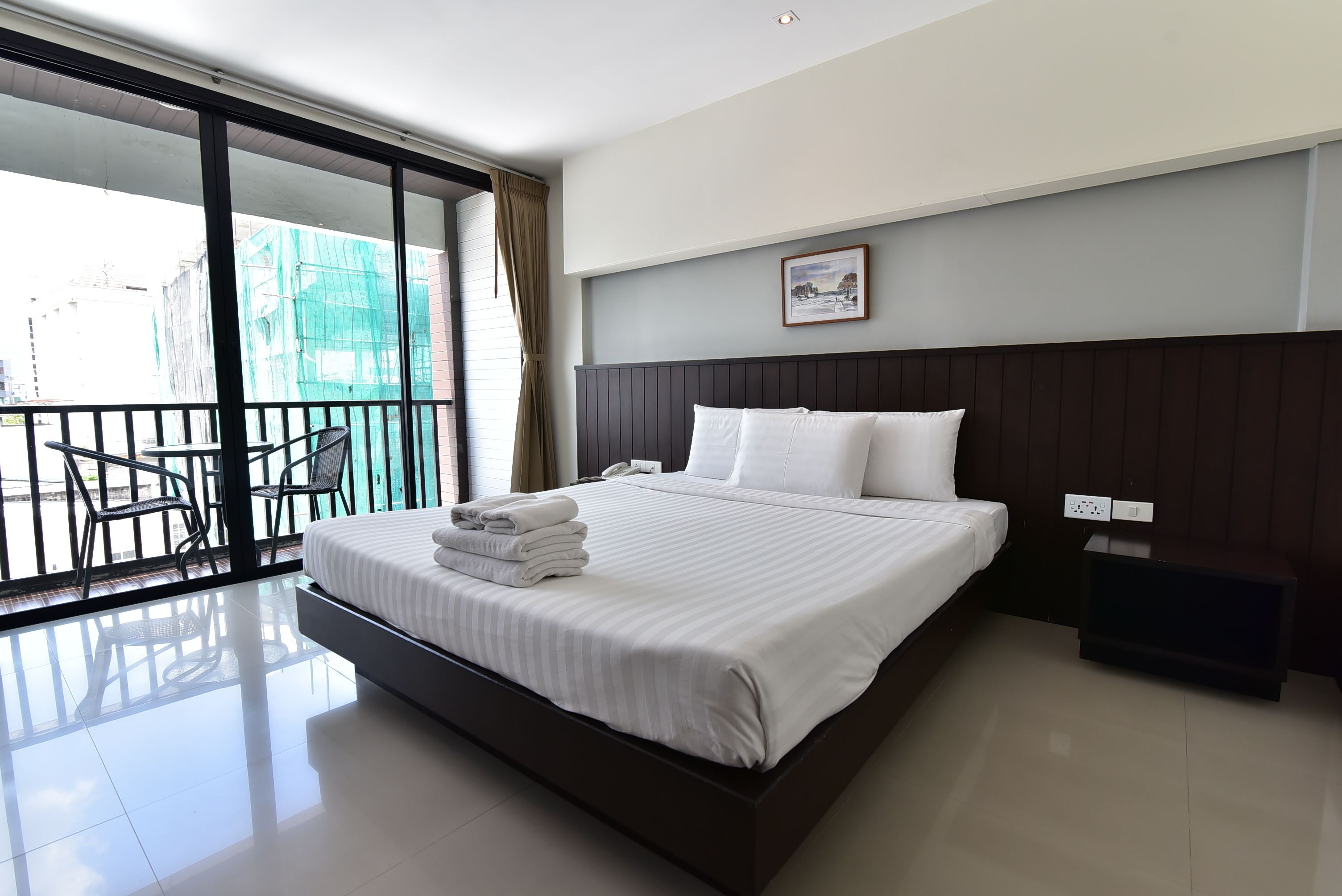 Une chambre d’hôtel moderne avec un grand lit, un balcon avec des chaises et une vue sur l’extérieur.