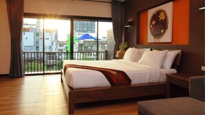 Quarto de hotel com uma cama grande, piso de madeira, varanda com vista para edifícios e um quadro na parede.