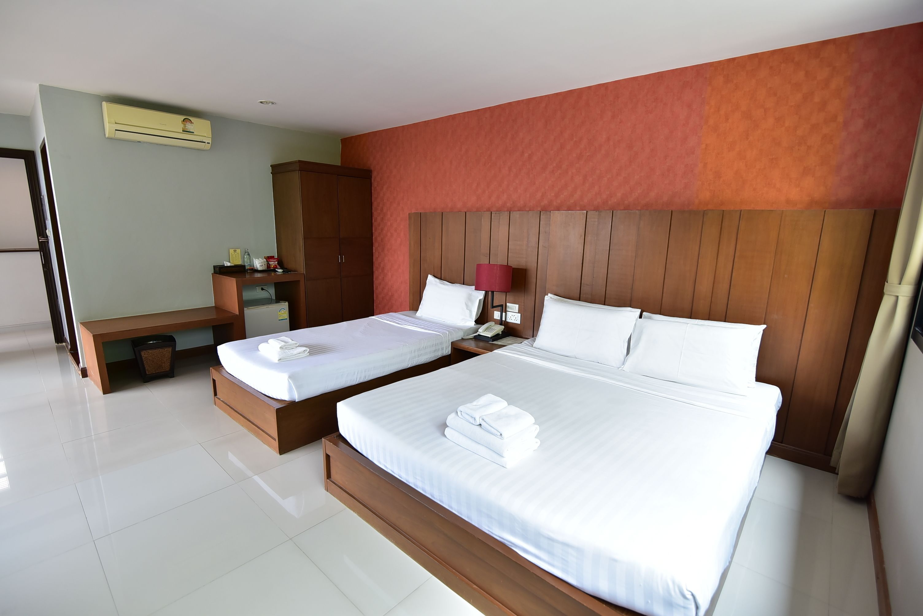 A hotel room with two beds, a wooden headboard, a desk, and a wardrobe.