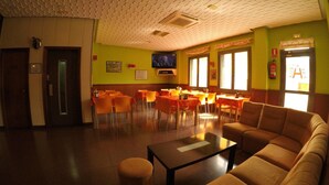 A dining area with tables and chairs, a sofa, and a television on the wall. - Hostal Palafox (Barbastro)