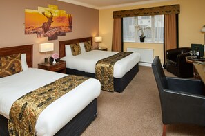 A hotel room with two beds, a desk, a chair, a window with curtains, a radiator, and a wall with a painting. - Eviston House Hotel (Killarney)