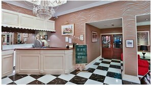 Eine Hotelhalle mit Schachbrettmuster-Boden, einer Rezeption und einer Kristallleuchter.