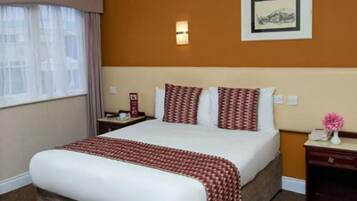 Une chambre d’hôtel avec un grand lit, une table de chevet, une commode, un tableau encadré au mur et une fenêtre avec des rideaux.