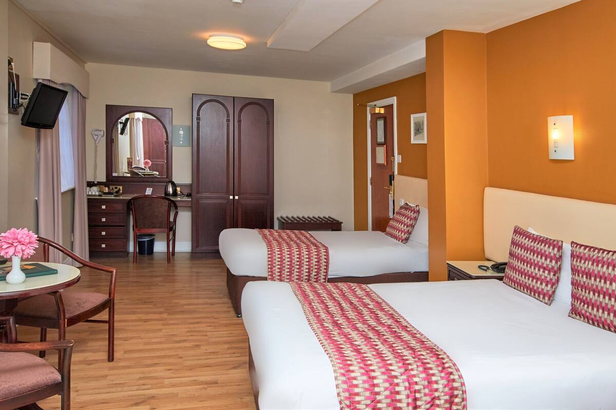 A hotel room with two beds, a desk, a chair, and a small table with a vase of flowers.