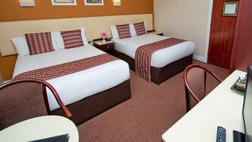 A hotel room with two beds, a desk, and a chair. There are framed pictures on the wall, a clock, and a door with a plaque.