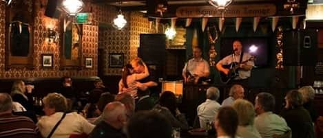 A bar with a band performing, patrons seated at tables, and a sign reading "The Bohemian Lounge".