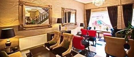 Een hotel lobby met een zwart-wit geruit vloerkleed, een grote spiegel en verschillende zithoeken.