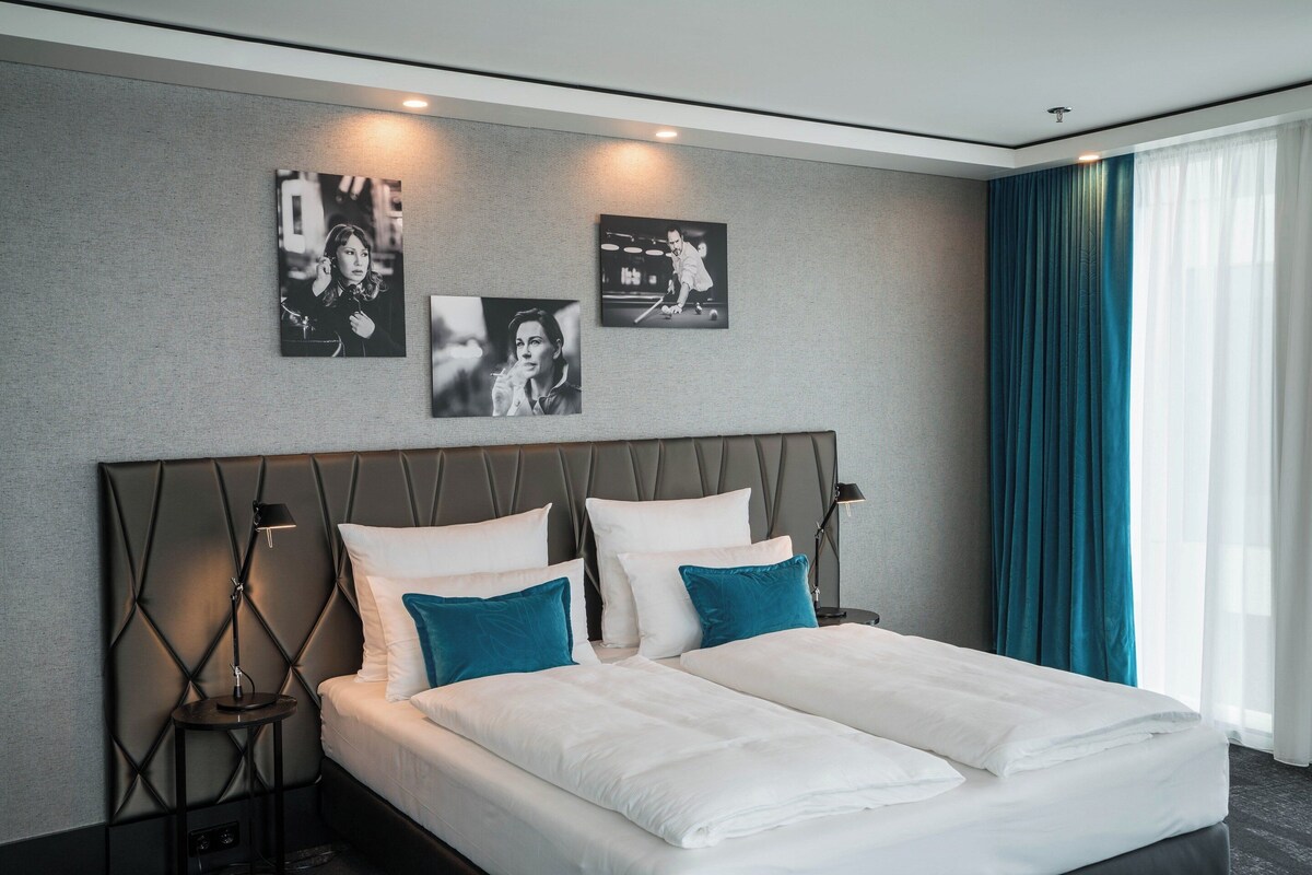 A modern hotel room with a large bed, two bedside tables, and wall-mounted artwork.