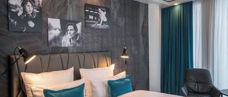 Habitación de hotel con una cama grande, dos lámparas de noche, una silla y un televisor montado en la pared.