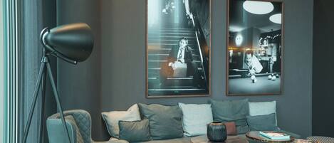 Un espace de détente moderne comprenant un ensemble de canapés, une lampe sur pied, une table basse ronde et deux photographies encadrées accrochées au mur.